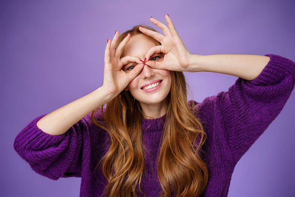 Hey smile more. Portrait of bright and funny charming redhead girl in purple sweater making mask with hands over eyes and smiling broadly acting like superhero posing excited and playful - Photo, Image