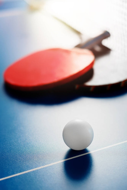 Zwei Tennisschläger und ein weißer Ball liegen auf einer Tischtennisplatte neben dem Netz. Aktive Erholung und Tischtennis spielen. - Foto, Bild