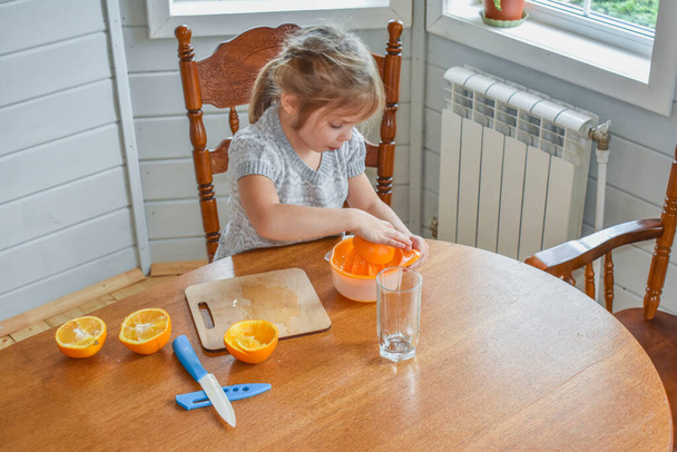 a child girl in the kitchen cuts and squeezes oranges juice - Foto, Bild
