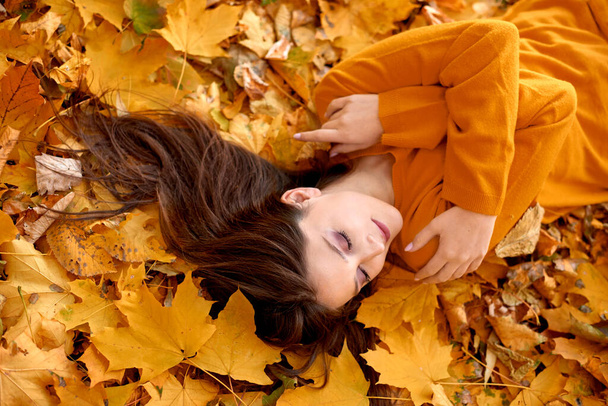 meisje ligt op de gevallen gele gebladerte in par of bos. concept van haarverzorging in de herfst. oppervlakkige scherptediepte - Foto, afbeelding