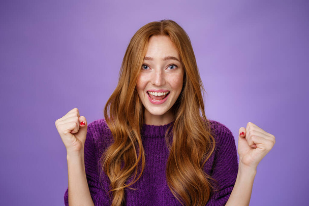 Optimistic, lucky young attractive female student winning trip around european smiling broadly from success and delight clench fists in triumph and celebration gesture, happy to win over purple wall - Photo, Image