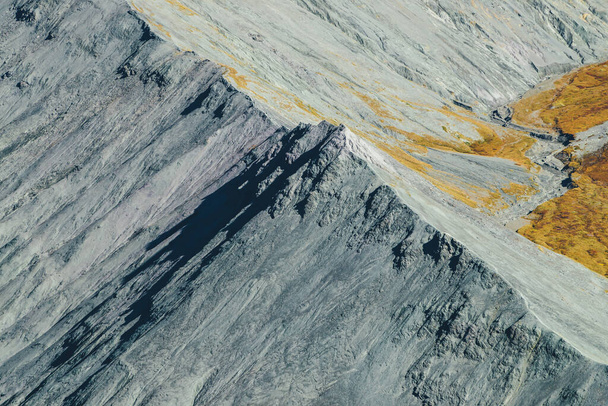 Ελάχιστο φθινοπωρινό τοπίο με γκρι βραχώδη μυτερή κορυφή στη λιακάδα. Εντυπωσιακή γραφική θέα από ψηλά σε απότομη κορυφογραμμή του βουνού το φθινόπωρο του χρόνου. Μινιμαλιστικό ορεινό τοπίο με βράχια και φθινοπωρινά χρώματα. - Φωτογραφία, εικόνα