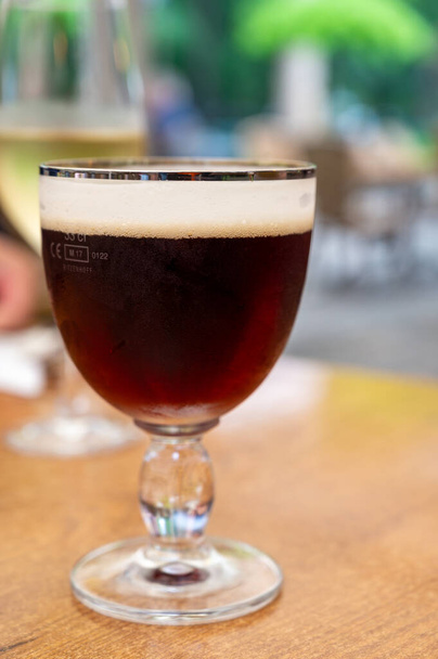 Стакан тёмного вкусного бельгийского дуббл-коричневого пива с пивоварни аббатства подается на открытом воздухе. - Фото, изображение