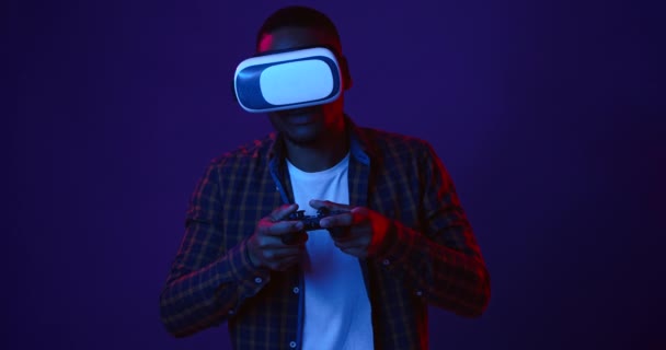 VR gambling. Young black guy playing video games with joystick and virtual reality headset, neon lights background - Footage, Video