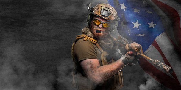 Επαγγελματίας στρατιώτης των ειδικών δυνάμεων, κατά τη διάρκεια ειδικής επιχείρησης σε καπνό πάνω σε σκοτεινό τσιμεντένιο τοίχο και φόντο της σημαίας των ΗΠΑ - υπερασπίζεται τη σημαία. Φωτογραφία με χώρο αντιγραφής - format 2x1. - Φωτογραφία, εικόνα