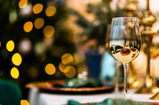 A beautiful glass with a golden coating stands on the New Year's table. Blurred background with bokeh. Photo - Zdjęcie, obraz