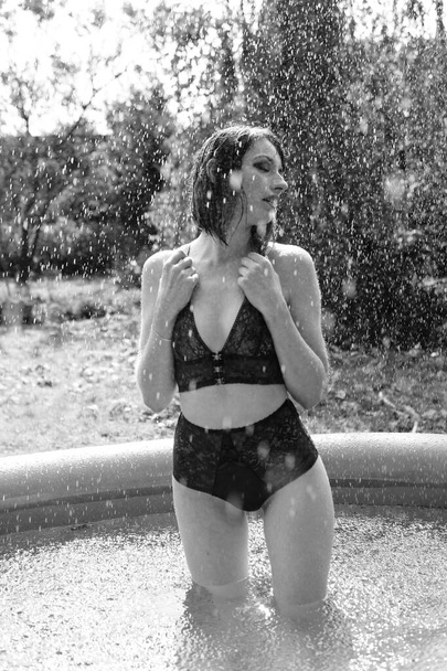 Beautiful woman in dark lingerie posing in swimming pool outdoor, black and white  - Photo, Image
