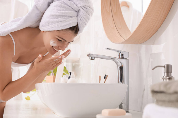 Beautiful teenage girl washing face with cleansing foam in bathroom. Skin care cosmetic - Фото, изображение