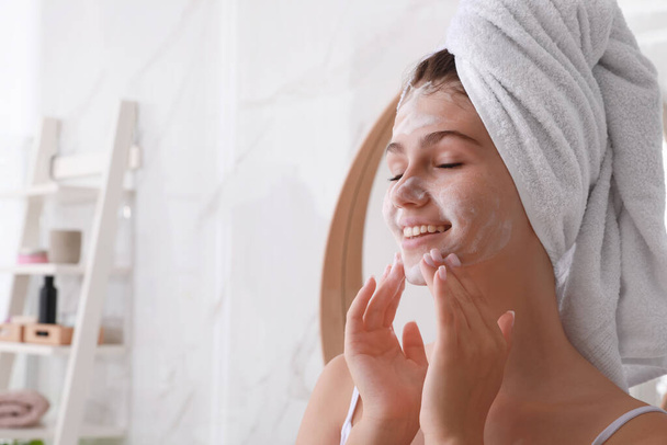 Beautiful teenage girl applying cleansing foam onto face in bathroom, space for text. Skin care cosmetic - Fotó, kép