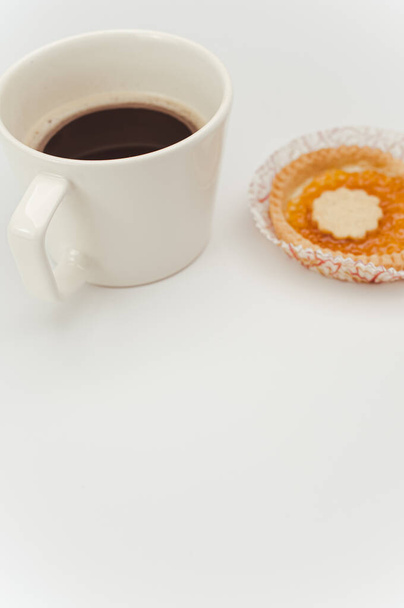 isolated apricot jam tart in a paper backing cup and cup of coffee on a white background with text space - Фото, зображення