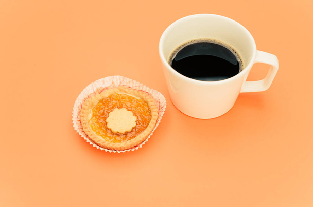 isolated apricot and cherry jam tart in a paper backing cup and cup of coffee on a orange background text space - Foto, immagini