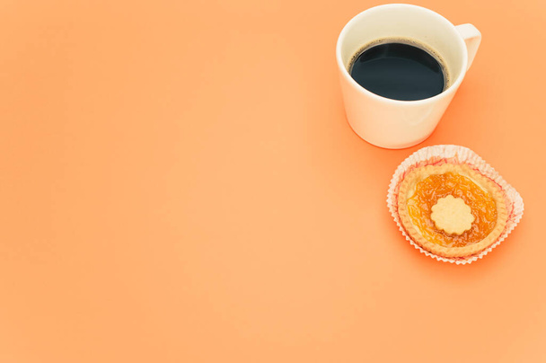 isolated apricot and cherry jam tart in a paper backing cup and cup of coffee on a orange background text space - Fotografie, Obrázek