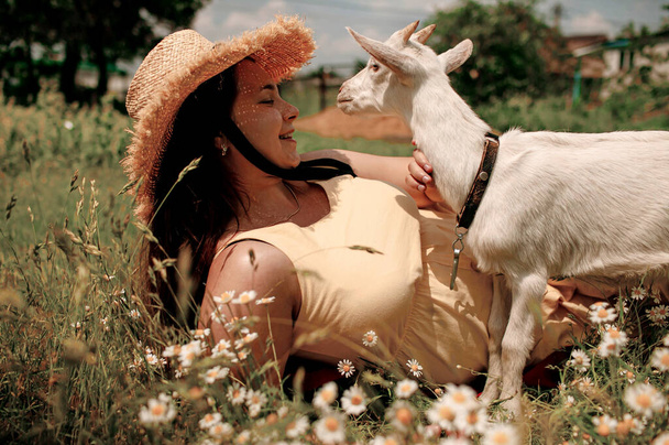 Animales del pueblo. Feliz mujer embarazada abraza cabra, concepto de unidad de la naturaleza y el hombre. La vida en el campo. - Foto, Imagen