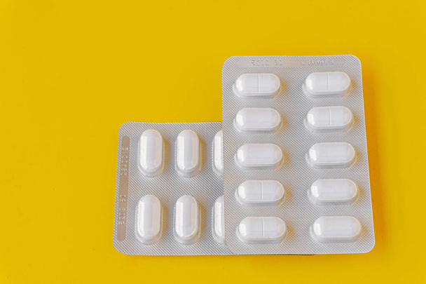 Enfoque selectivo en algunos blisters con pastillas blancas aisladas sobre fondo amarillo, concepto de medicina.  - Foto, Imagen