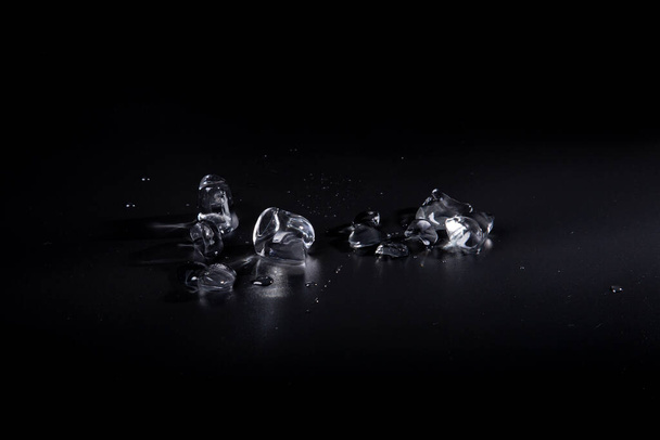 pieces, fragments of transparent ice on a black background. Chunks of ice in puddles of water on background. View of ice from above. - Φωτογραφία, εικόνα