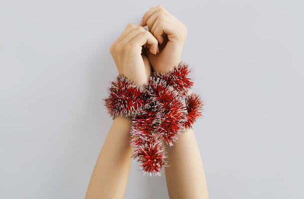 Beautiful women's hands are tied with a decorative Christmas garland on a gray background. Red tinsel for the Christmas tree is wrapped on the hands of a young girl. The concept of New Year holidays - Foto, Bild