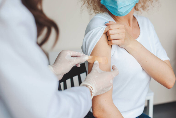 Az orvosi nővér tapaszt tett egy fiatal nő karjára, miután beadta neki a koronavírus vakcinát. Vírusellenes vakcina. - Fotó, kép