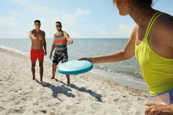 Friends playing with flying disk at beach on sunny day - Foto, Bild