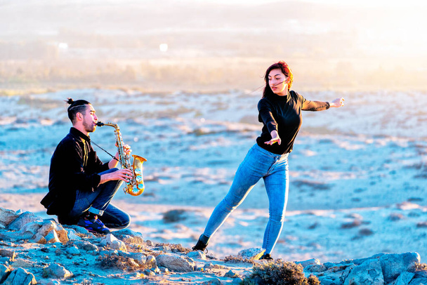 latynoski muzyk gra na saksofonie, podczas gdy latynoska kobieta tańczy na pustynnym krajobrazie - Zdjęcie, obraz