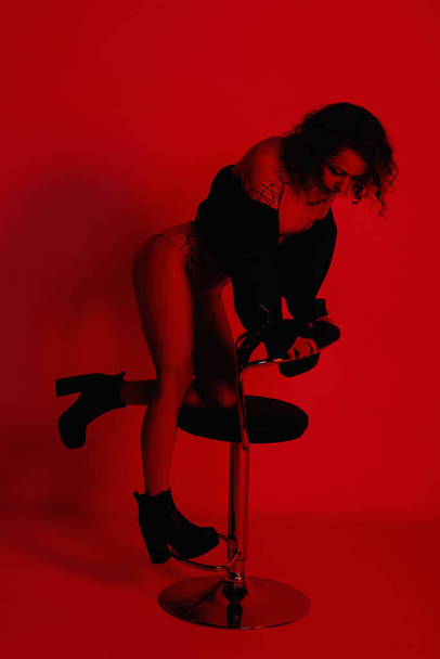 Μοντέλα μόδας με κομψά ρούχα στα φώτα νέον στο στούντιο. Πορτραίτο στούντιο μιας σέξι γυναίκας με δερμάτινο μπουφάν, κορμάκι και μπότες σε κόκκινο υπεριώδες φόντο σε νυχτερινό κέντρο διασκέδασης - Φωτογραφία, εικόνα