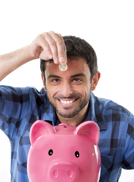 young happy man holding coin putting it into pink piggy bank - Photo, Image