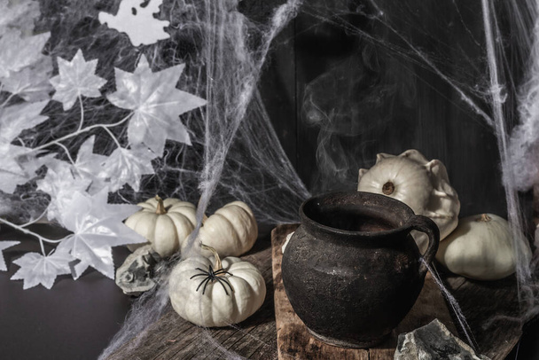 Halloween ünnep. Ünnepi kompozíció boszorkányfazékkal, sütőtökkel, denevérrel, szellemmel, pókokkal és pókhálókkal. Világos füst, fekete-fehér tónusok, ünnepi szellem - Fotó, kép