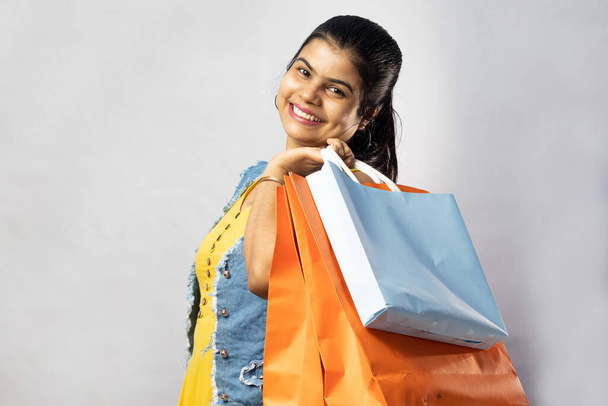 Uma bela mulher indiana em vestido amarelo com sacos de compras olhando para a câmera no fundo branco - Foto, Imagem