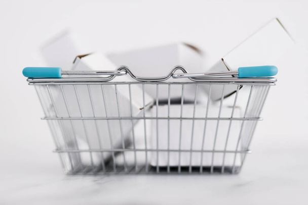 shopping and add to cart concept, parcels of different shapes piled up inside of shopping basket on light marble background shot at shallow depth of field - Photo, Image