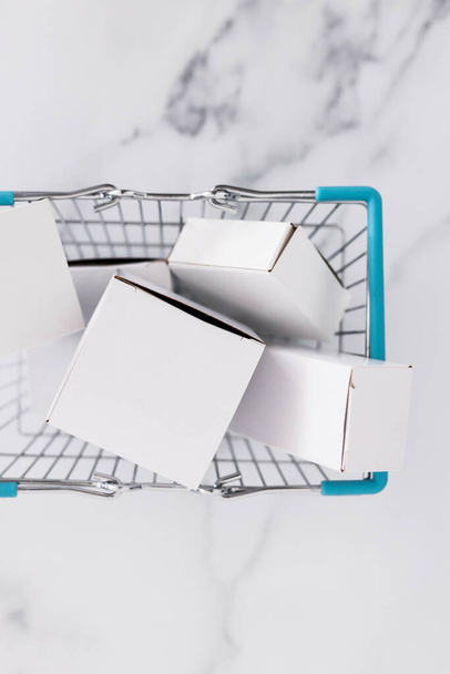 shopping and add to cart concept, parcels of different shapes piled up inside of shopping basket on light marble background shot at shallow depth of field - Photo, image