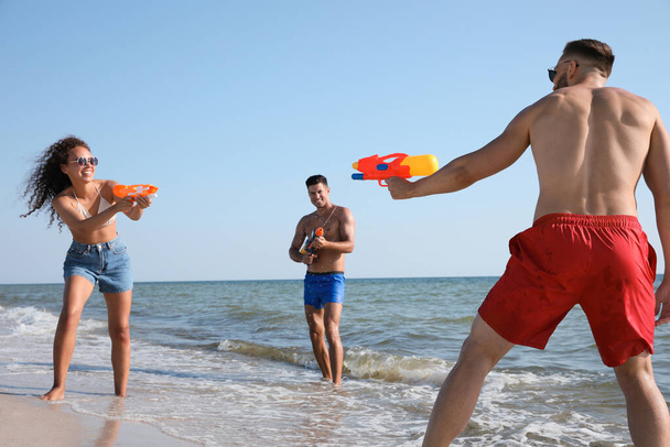 Friends with water guns having fun on beach - 写真・画像
