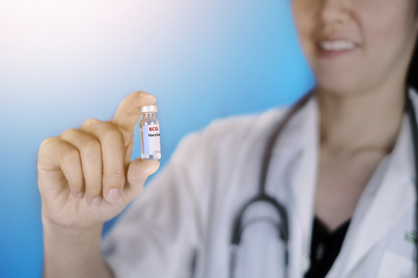 Ένας γιατρός με λευκό παλτό και στηθοσκόπιο γύρω από το λαιμό της κρατά ένα γυάλινο μπουκάλι με εμβόλιο BCG που αποτρέπει τη φυματίωση, ένα είδος βακτηριακής λοίμωξης. Υγεία και ιατρική έννοια. - Φωτογραφία, εικόνα