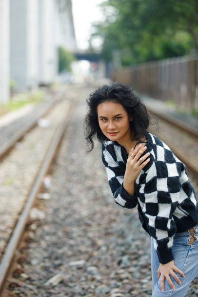 Portrait of 20s Asian Woman brown hair wear jacket high fashion make up under blue sky cloud. Beautiful female express feeling emotion smile happy over train track railroad station - Photo, Image