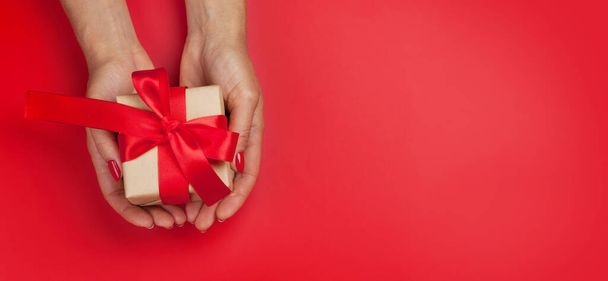 Woman hands holding Christmas or Valentine's Day gift box on red background. Top view flat lay with copy space - Zdjęcie, obraz