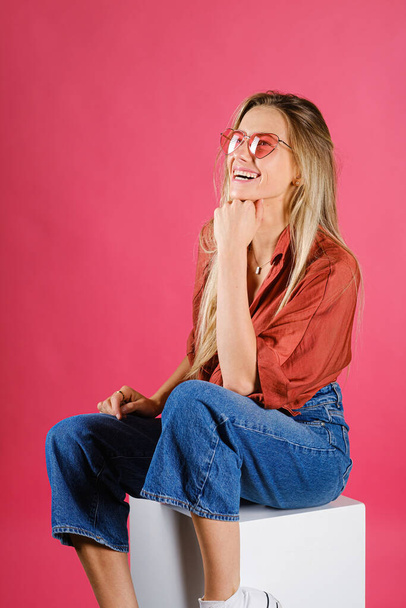 A vertical shot of an attractive Caucasian female wearing a red shirt and glasses against a pink wall - Фото, зображення