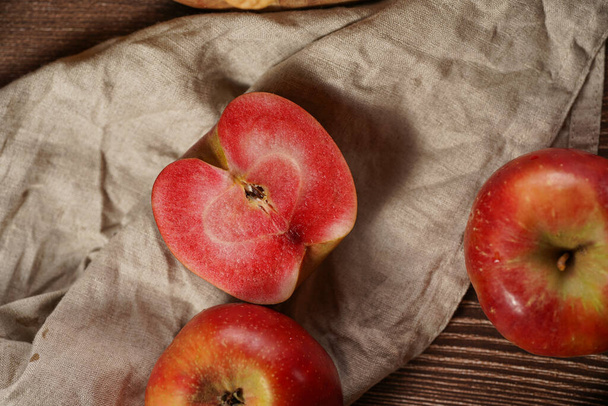 Mehrere ganze und geschnittene Äpfel und Apfelhälften mit rotem Fruchtfleisch auf einem Leinentuch auf einem Holztisch - Foto, Bild