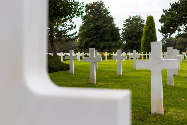 Amerykański cmentarz na plaży Omaha, patrząc na białe krzyże grobowe i nieostry krzyż na pierwszym planie - Zdjęcie, obraz