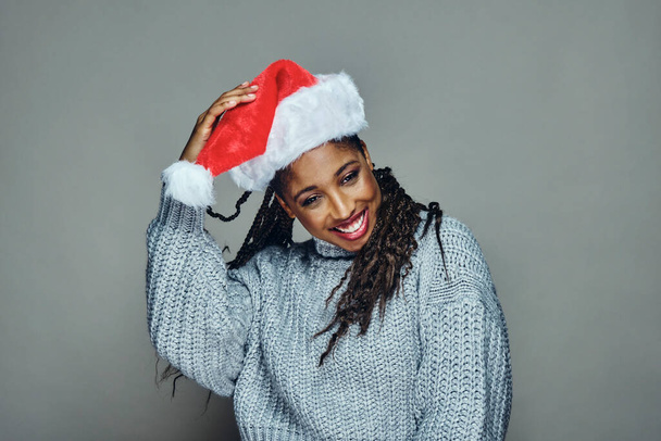Cheerful young woman wearing Santa hat and sweater against gray background - Фото, зображення