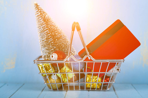 Shopping basket with Christmas gifts, decor and credit card on a blue wooden background. Christmas sale. - Fotoğraf, Görsel