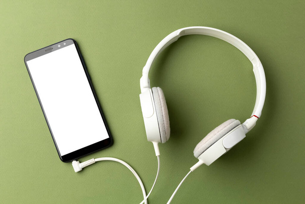smartphone con auriculares sobre fondo verde, escucha audiolibros o música con auriculares - Foto, imagen