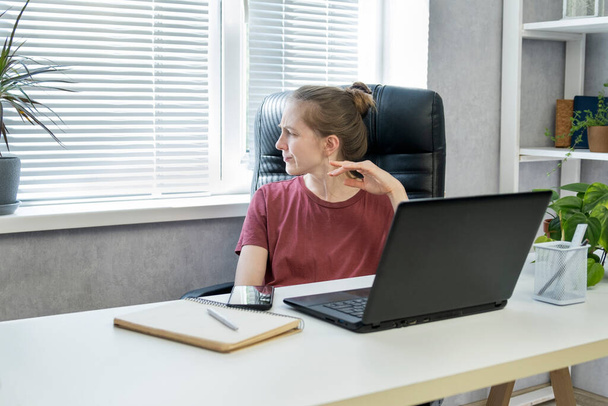 机の上の若い女性がプロジェクトのことを考えている。オフィスにはノートパソコンと日記を持つビジネス女性が座っています - 写真・画像