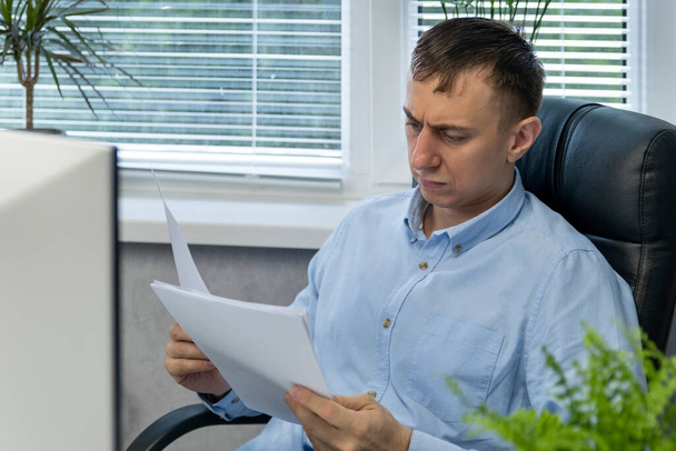 Zaostřený kancelářský pracovník čte dokumenty a kousá do skleněného oblouku. Mužský účetní. Asistent ředitele - Fotografie, Obrázek