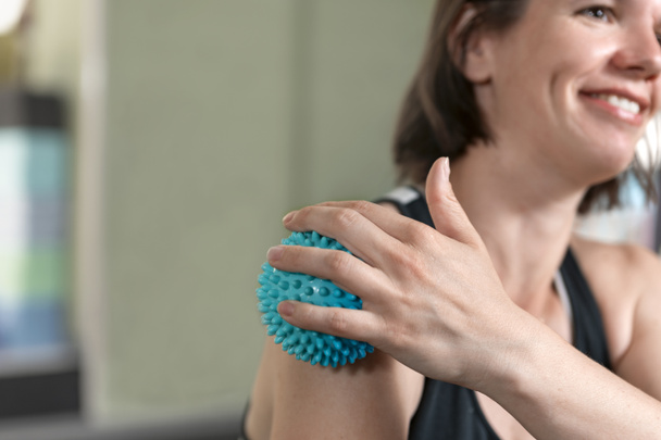 Young woman massages her shoulder with an MFR ball. Myofascial roll. Roller for physiotherapy - Photo, Image