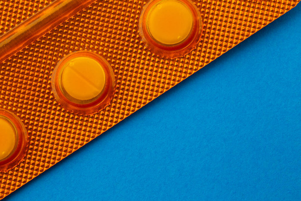 Pills in blisters presented against a blue background. Photo taken under artificial light - Fotografie, Obrázek