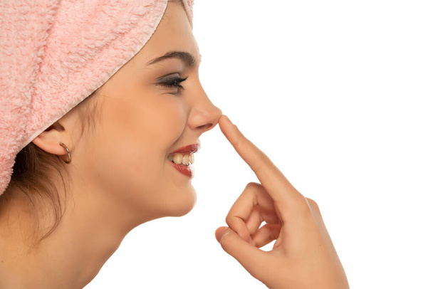 Profilo pf una giovane donna sorridente con un asciugamano sulla testa, si tocca il naso su uno sfondo bianco - Foto, immagini