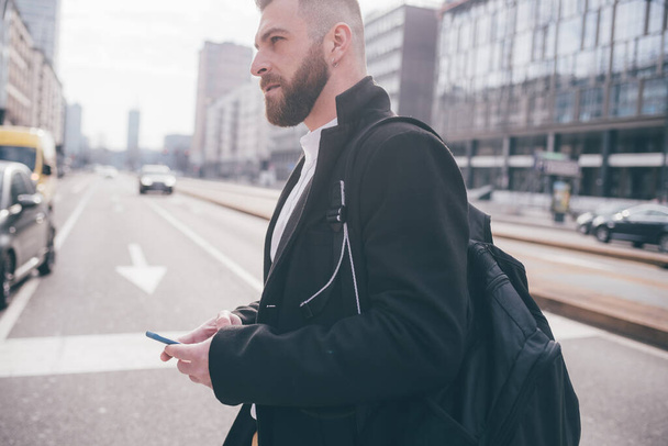 Jeune homme caucasien adulte barbu marchant à l'extérieur en utilisant smartphone navigation web télétravail vérification email - Photo, image