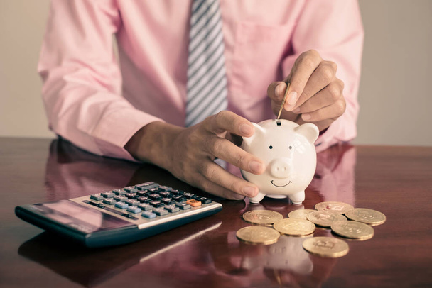 The hand of a businessman puts coins in a piggy bank, saves money with coins, steps into a successful growth business, and saves for retirement concept. - Foto, Imagen