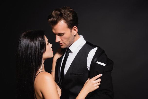 passionate woman undressing man in elegant suit isolated on black - Photo, Image