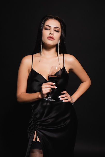elegant woman with glass of red wine posing with hand on hip isolated on black - Фото, зображення