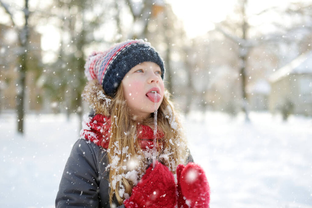Adorable young girl having fun in beautiful winter park during snowfall. Cute child playing in a snow. Winter activities for family with kids. - Foto, Imagen