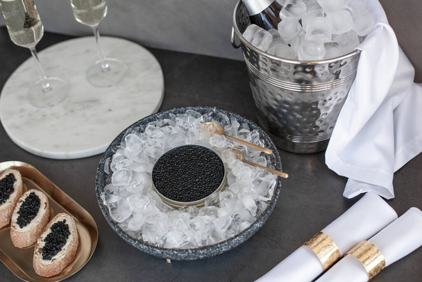 Black caviar in can on ice, caviar sandwich on golden plate, champagne in glass - Фото, изображение